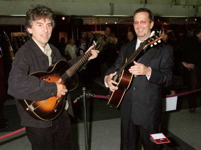 George Harrison y Eric Clapton, fotografiados mientras tocaban sus guitarras en una subasta benéfica en 1999. Harrison moriría dos años después.