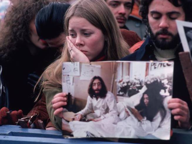 Una multitud de fans lamenta el asesinato de John Lennon en Central Park, Nueva York, sujetando una foto del exbeatle y d esu mujer, Yoko Ono, en diciembre de 1980.