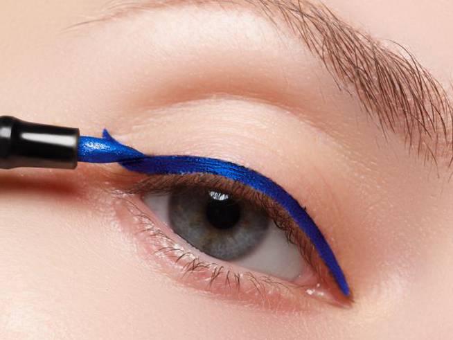 Una chica pintándose el eyeliner azul.