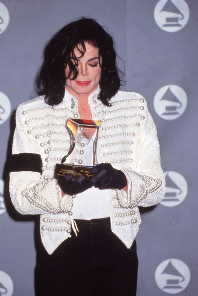 Michael Jackson sostiene su Grammy a Leyenda en los Grammy de 1993. La chaqueta que escogió aquel día simula la de un unifrome militar pero los detalles están elaborados con perlas.