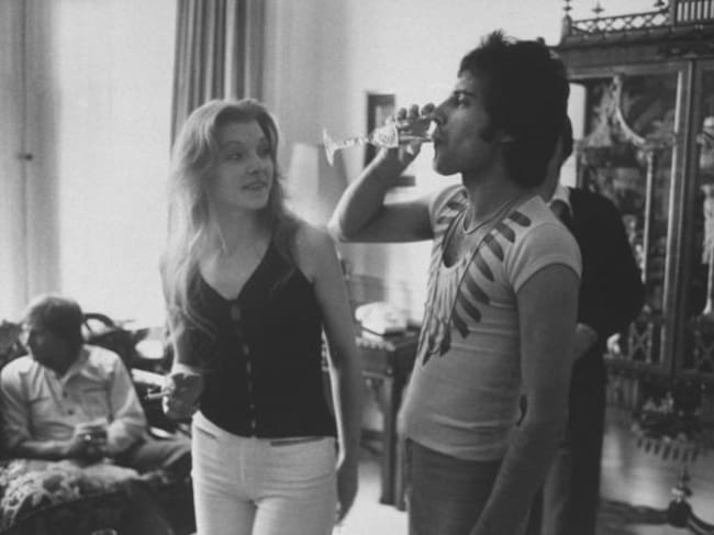 Rock singer Freddie Mercury bebe una copa de champán junto a su entonces novia Mary Austin .