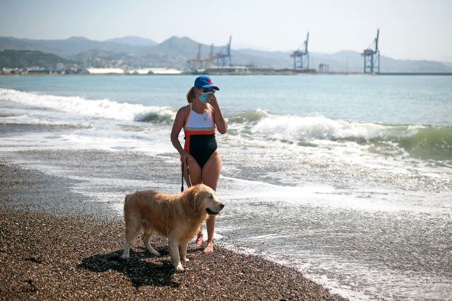 Una mujer pasea con su perro por una playa de Málaga.