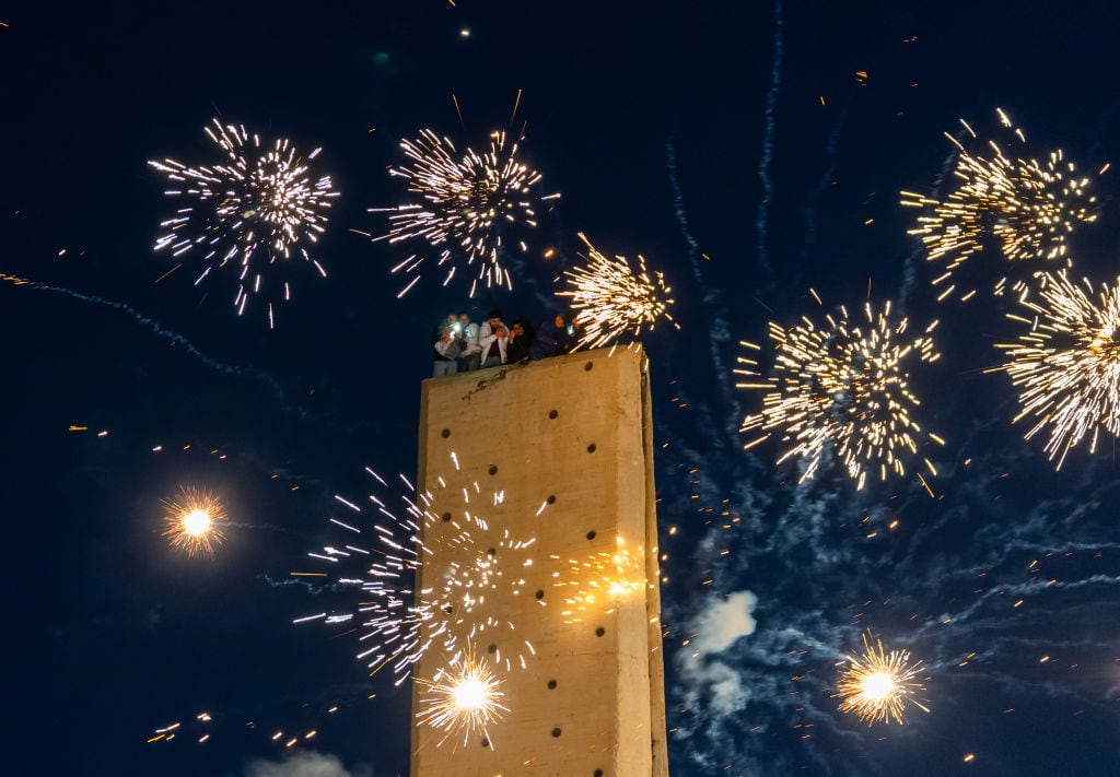 DAMASCUS, SYRIA - DECEMBER 13: Fireworks light up the night sky as people gather in Umayyad Square to celebrate the collapse of the 61-year-long Baath regime and the end of the Assad family era in Damascus, Syria on December 13, 2024. People climbed structures, waving flags and capturing the moment on their phones. (Photo by Emin Sansar/Anadolu via Getty Images)