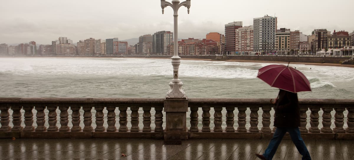Un hombre camina por el paseo marítimo de Gijón, en Asturias, bajo la lluvia