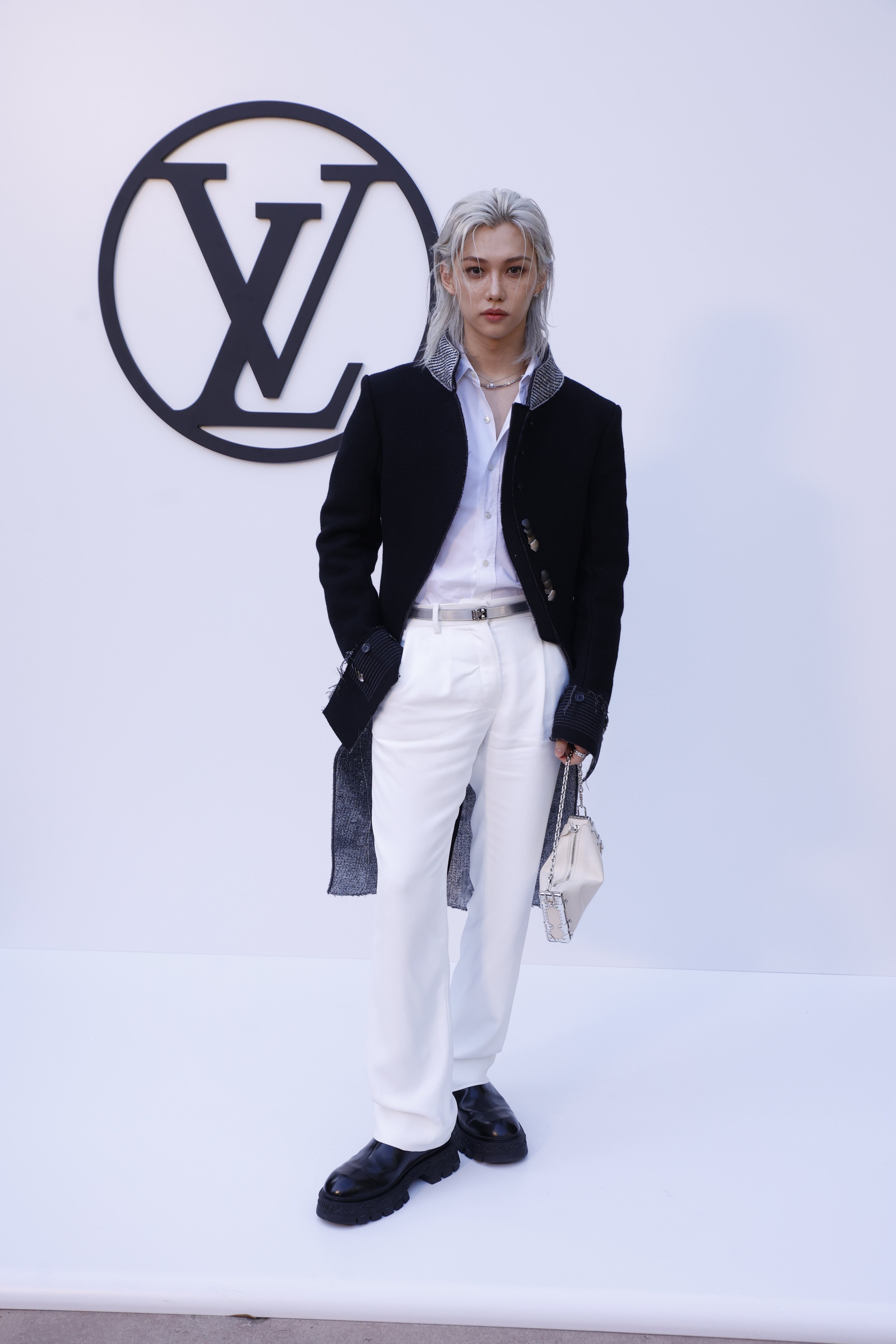 El cantante de K-Pop del grupo Stray Kids ha dejado claro que los bolsos no son solo para ellas y Louis Vuitton aboga por ello. Ha llegado con su larga melena rubio platino a juego con su camisa y pantalón de blanco impoluto. El contraste lo ponía el abrigo con detalles brillantes en el cuello.