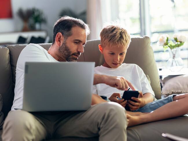Un padre y un hijo con dispositivos tecnológicos. / Getty