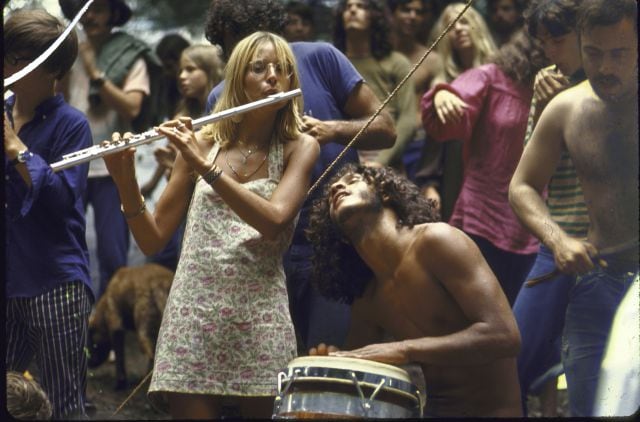 Asistentes al festival Woodstock bailan y tocan el timbal y la flauta travesera.