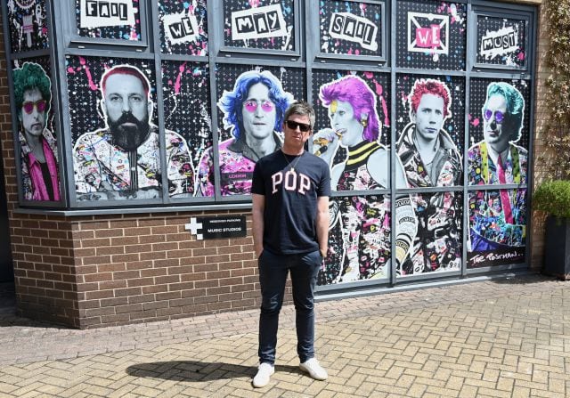 Noel Gallagher posa delante del mural en el que que están sus músicos favoritos: Bob Dylan, Andy Weatherall, David Bowie, John Lydon, John Lennon y Tony Wilson.