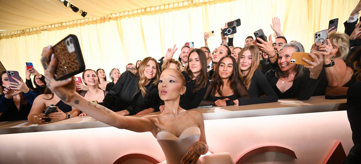Ariana Grande posando en la alfombra roja de los Oscars 2025 con un grupo de fans