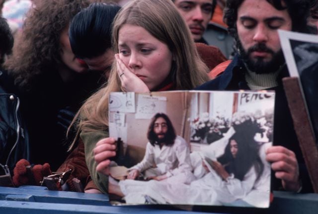 Una multitud de fans lamenta el asesinato de John Lennon en Central Park, Nueva York, sujetando una foto del exbeatle y d esu mujer, Yoko Ono, en diciembre de 1980.