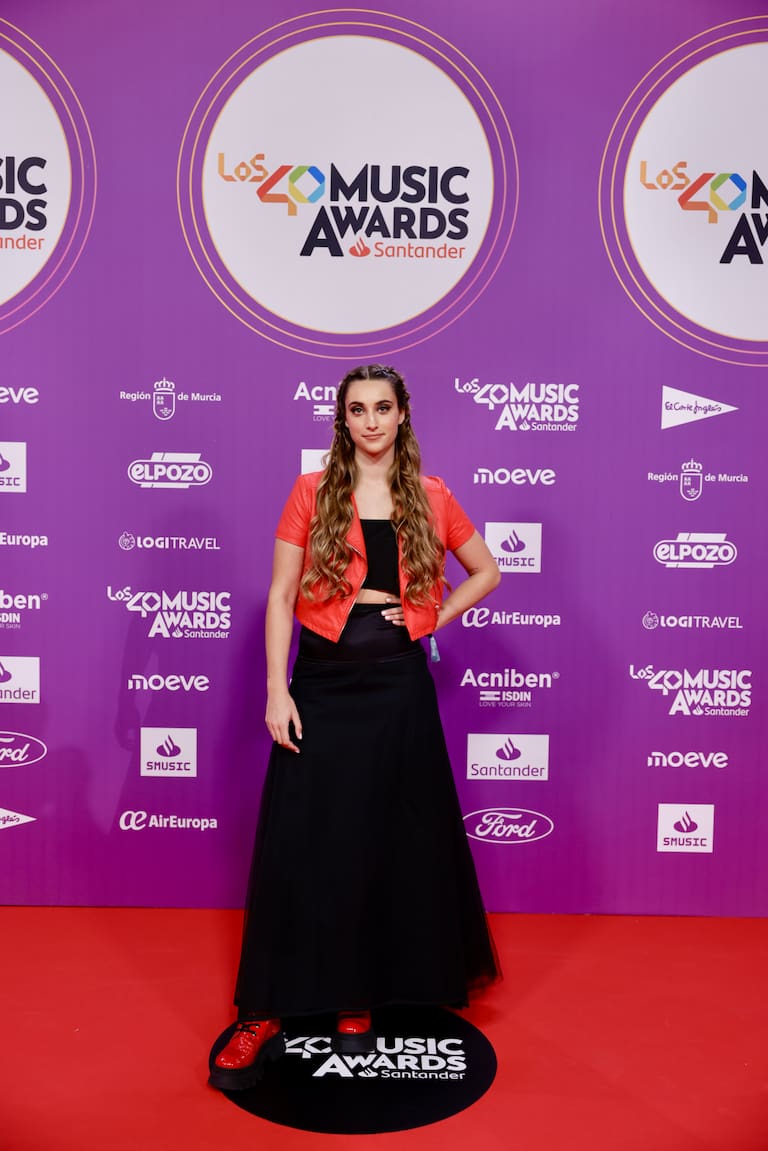 Aitana Jerez, locutora de LOS40 Urban, se une la alfombra roja de LOS40 Music Awards Santander 2025 con un conjunto dos piezas en negro y una torera en color rojo coral.