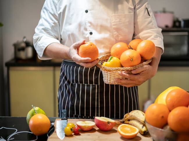 Un cocinero sostiene un frutero con naranjas