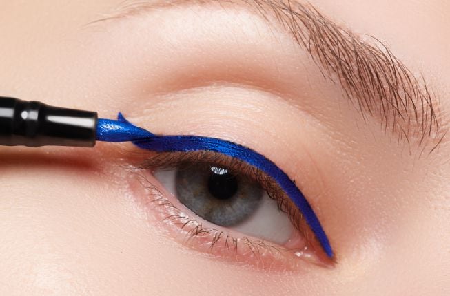 Una chica pintándose el eyeliner azul.