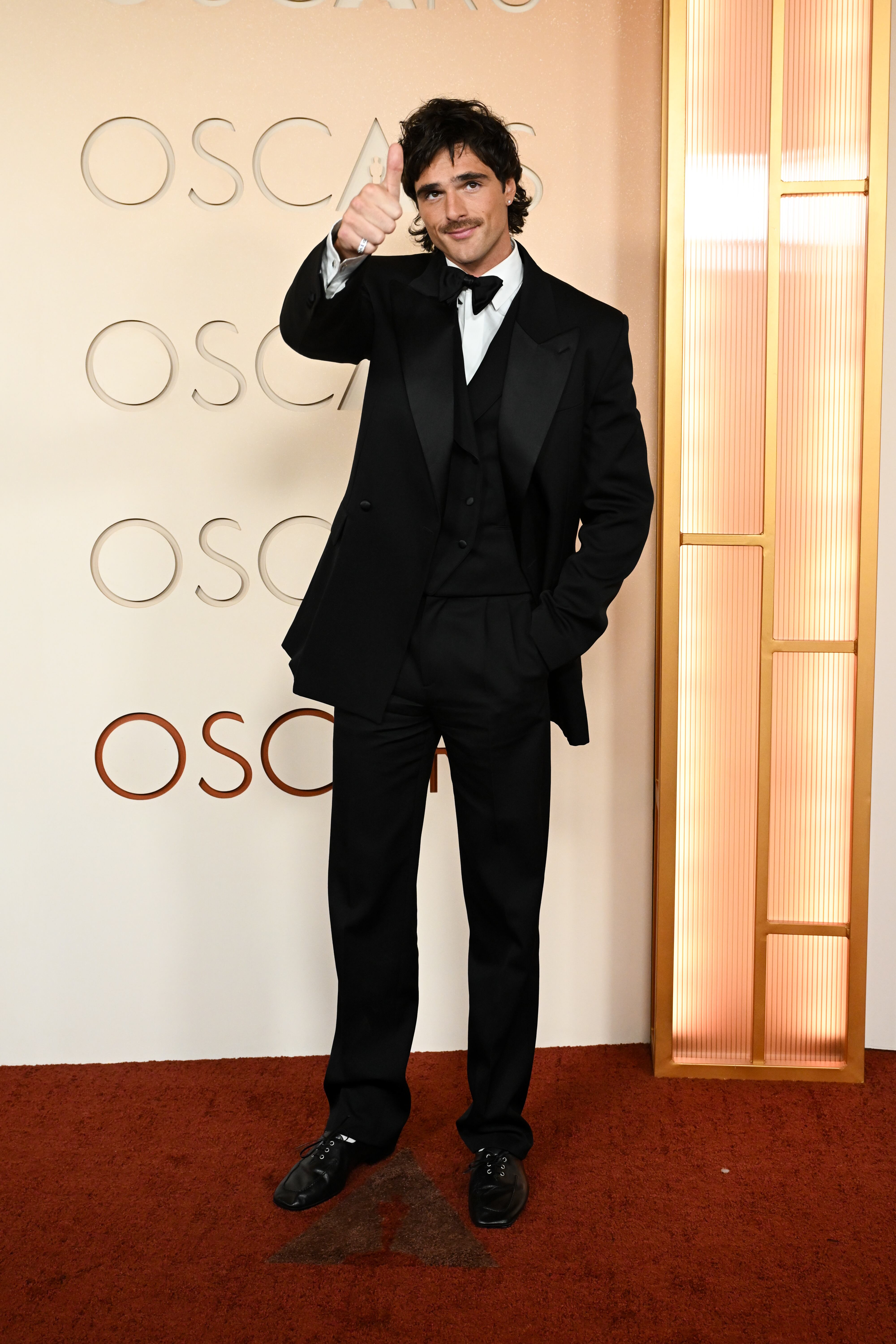 Nominado a mejor actor de reparto por Frankenstein, Jacob Elordi llegaba con su firma de cabecera esta temporada: Bottega Veneta. Elegante esmoquin negro tres piezas con solapa de raso, chaleco con doble botonadura y zapatos de cordones negros.