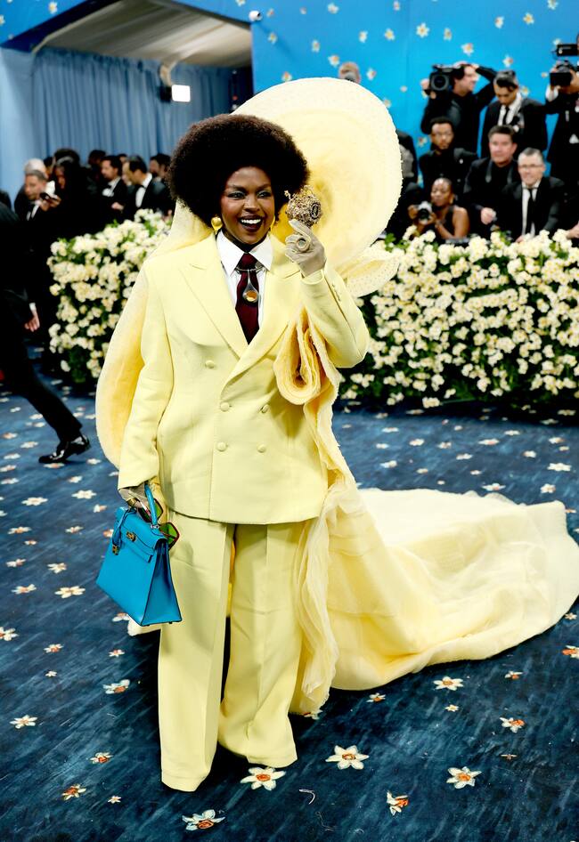 Parece mentira, pero sí, a sus 49 años, Lauryn Hill ha experimentado su primera MEG Gala y lo ha hecho con el color amarillo mantequilla con este traje con chaqueta cruzada y pantalones anchos. La chaqueta lucía una capa escultural que se curvaba como una corona alrededor de su altísimo afro antes de rodear su hombro izquierdo y convertirse en una capa con cola que rozaba el suelo. Contrastó el color con el azul del Birkin de Hermès.