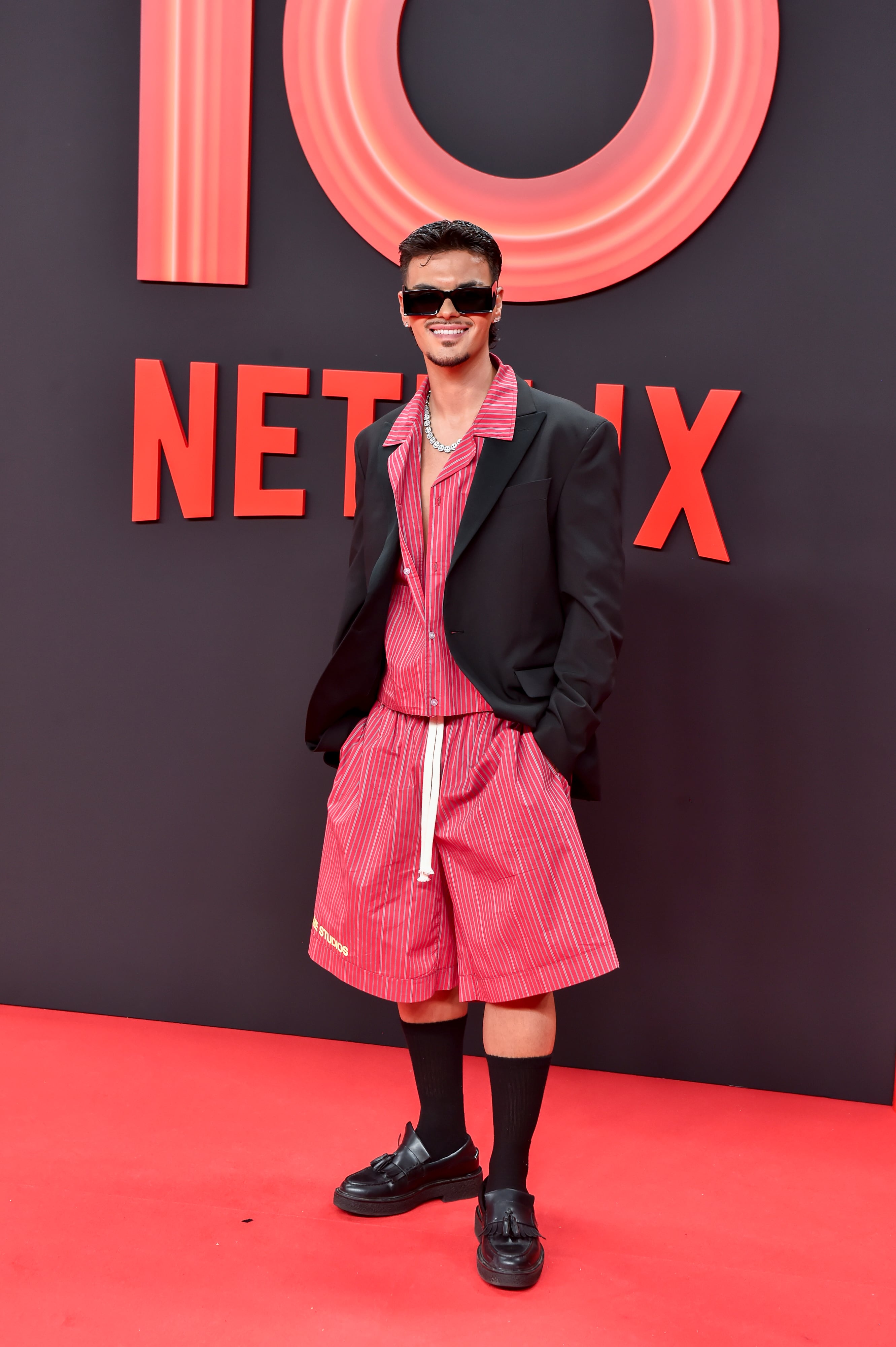 Curiosa combinación de Abraham Mateo con ese dos piezas de bermuda y camisa casual en rojo -o rosa- con chaqueta negra. No a todo el mundo le hubiera funcionado algo así.