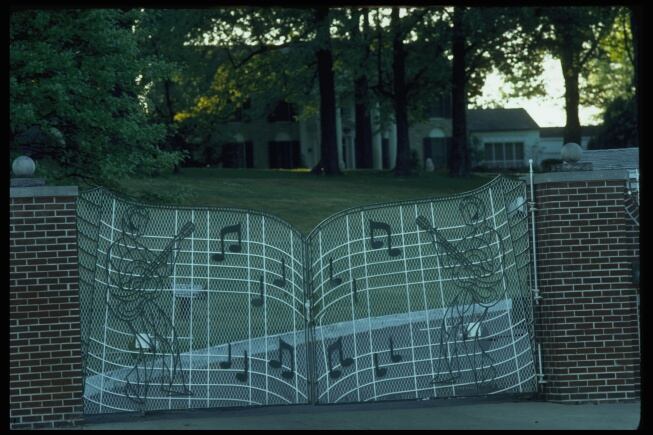 Imagen exterior de la mansión de Elvis, en Memphis, Tennessee. La valla de Graceland está decorada con notas musicales y dos guitarristas.