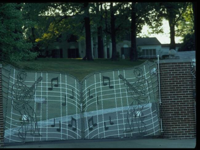 Imagen exterior de la mansión de Elvis, en Memphis, Tennessee. La valla de Graceland está decorada con notas musicales y dos guitarristas.