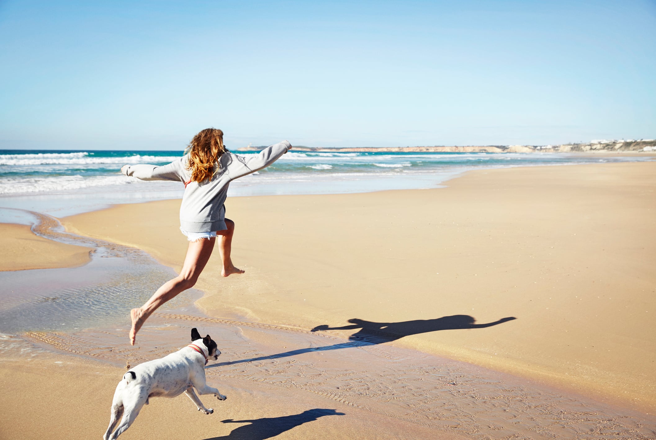 La dueña corriendo con su perro en la playa.