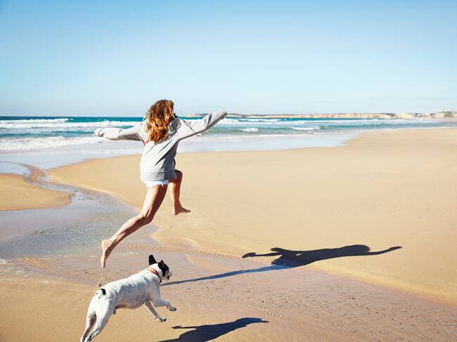 La dueña corriendo con su perro en la playa.