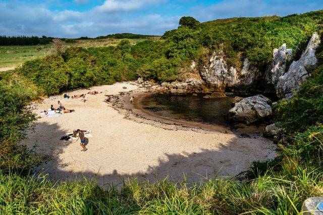 Varias personas toman el sol en la playa interior de Gulpiyuri, en Llanes, Asturias