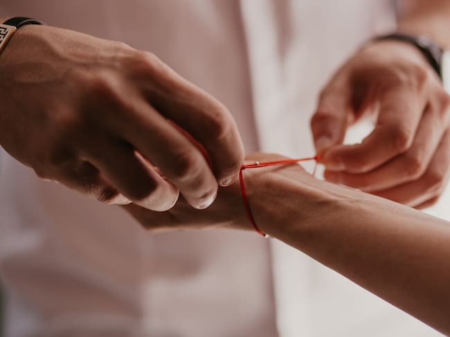 Una persona atándose un hilo rojo en la muñeca