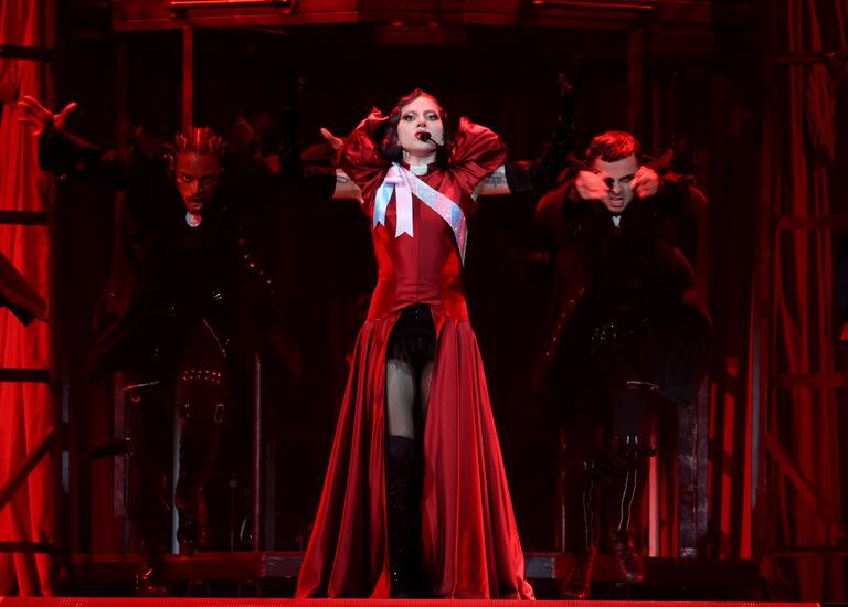 Lady Gaga durante su gira &#039;The MAYHEM Ball Tour&#039; en el Kia Forum de Inglewood, California. Gaga luce un vestido satinado rojo con una apertura en el frontal. El detalle del encaje negro y la banda en blanco hacen que el look sea muy teatral.
