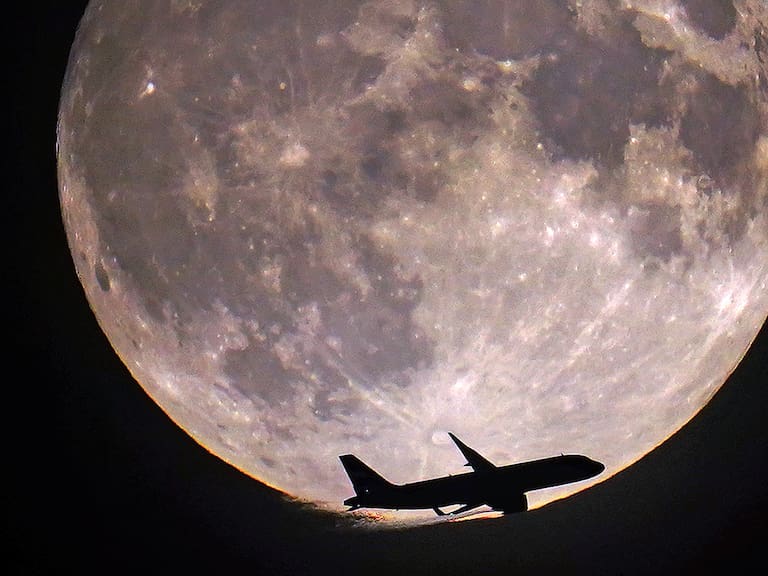 Un avión vuela con la Superluna Azul de 2023 de fondo.