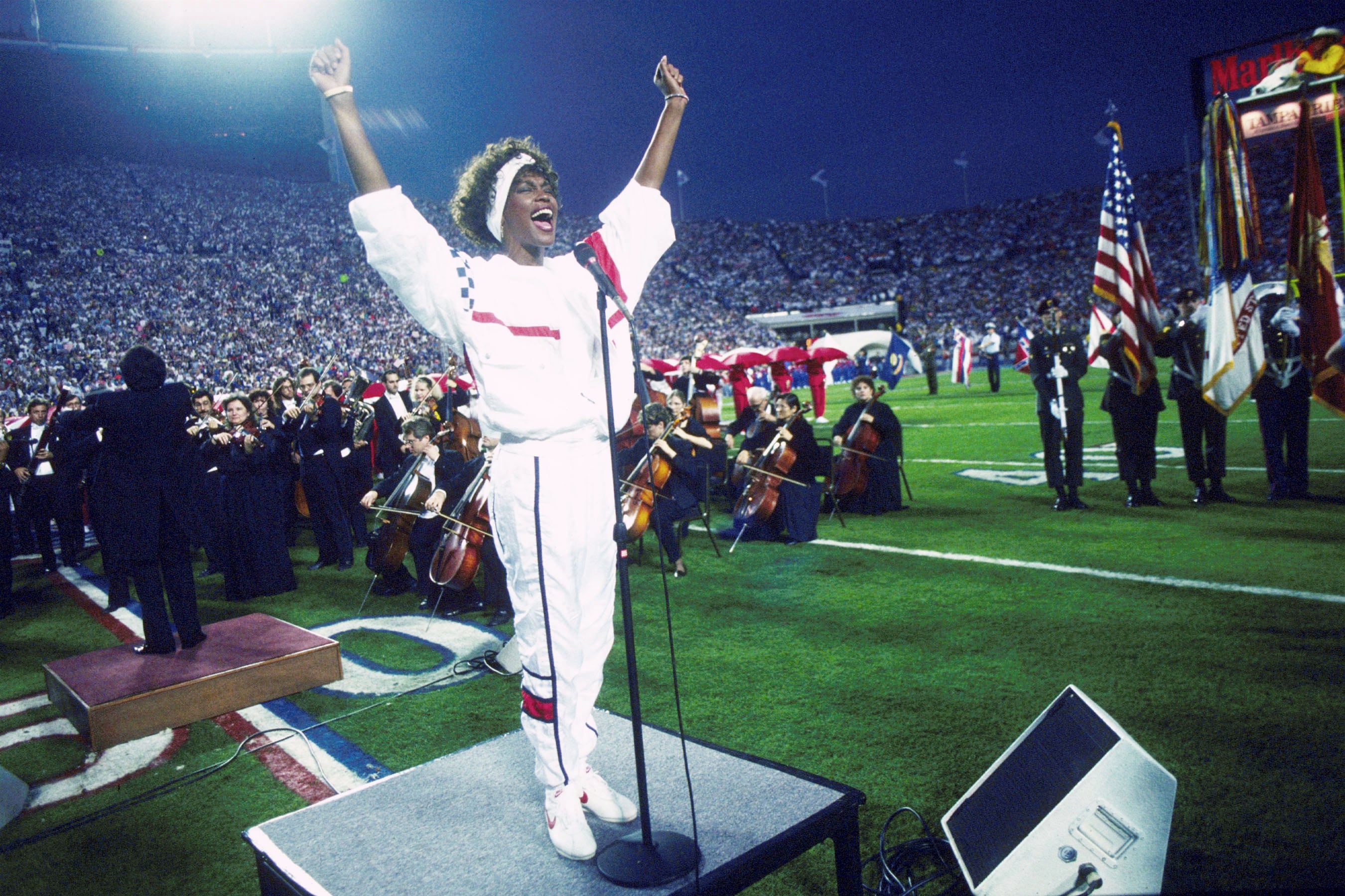 TAMPA, FL - 27 DE ENERO: Whitney Houston canta el himno nacional durante el espectáculo previo al Super Bowl XXV, mientras decenas de miles de aficionados al fútbol americano ondean pequeñas banderas estadounidenses en una increíble muestra de patriotismo durante la Guerra del Golfo Pérsico, el 27 de enero de 1991. (Foto de Michael Zagaris/Getty Images)