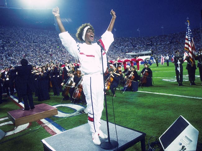TAMPA, FL - 27 DE ENERO: Whitney Houston canta el himno nacional durante el espectáculo previo al Super Bowl XXV, mientras decenas de miles de aficionados al fútbol americano ondean pequeñas banderas estadounidenses en una increíble muestra de patriotismo durante la Guerra del Golfo Pérsico, el 27 de enero de 1991. (Foto de Michael Zagaris/Getty Images)