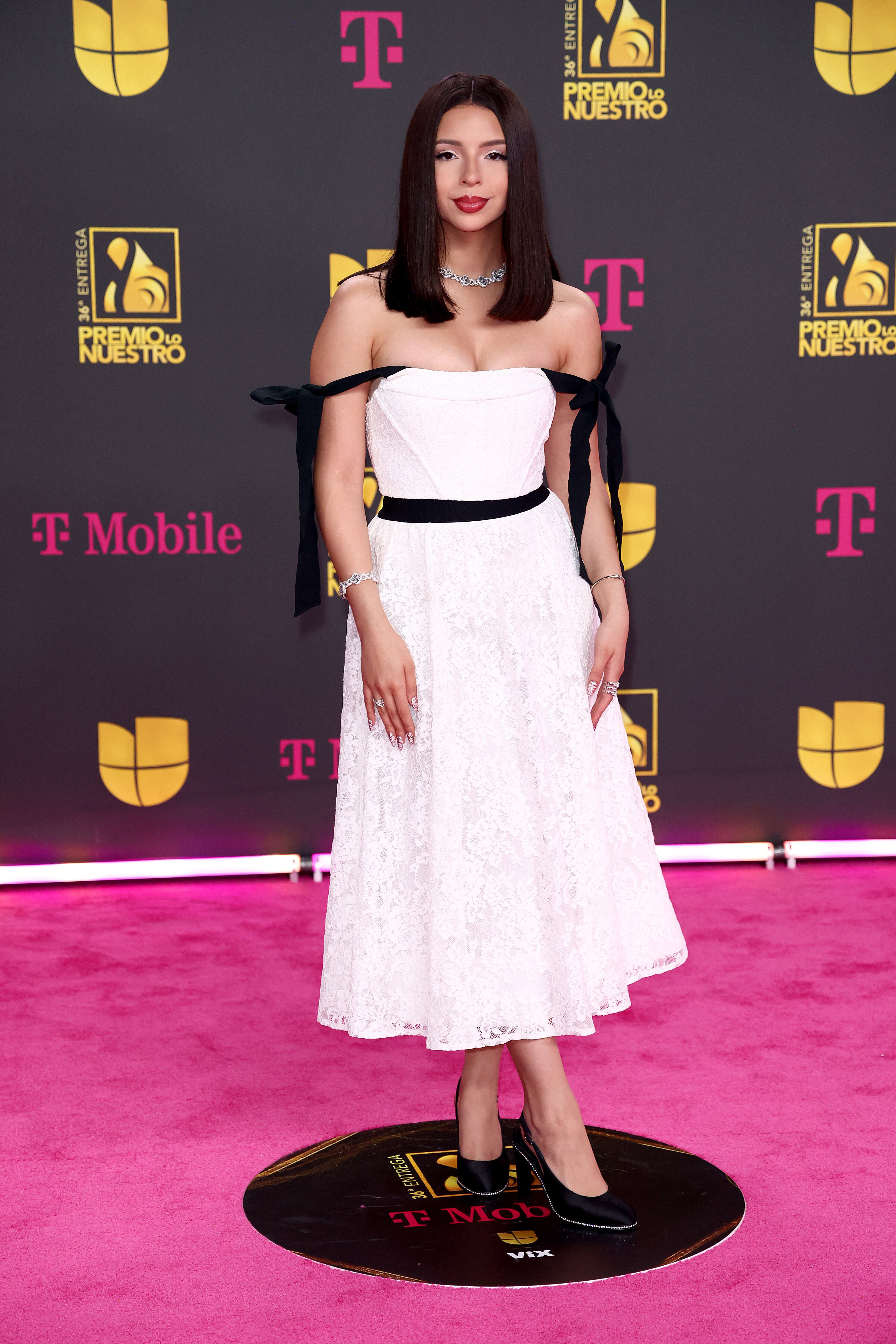 Ángela Aguilar se ha convertido en una habitual de las galas latinas y es que su música mexicana enamora, como sus estilismos preppy, en esta ocasión un vestido midi en blanco con lacitos negros, muy coquette, tendencia en alza.
